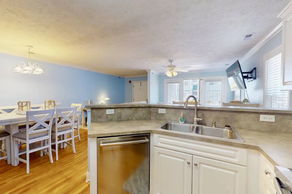 A welcoming kitchen scene includes a kitchen sink, dining table, ceiling fan, and television, with visible cabinetry hinting at ample storage space. The area feels bright and ready for use, suggesting everyday convenience and practical amenities.
