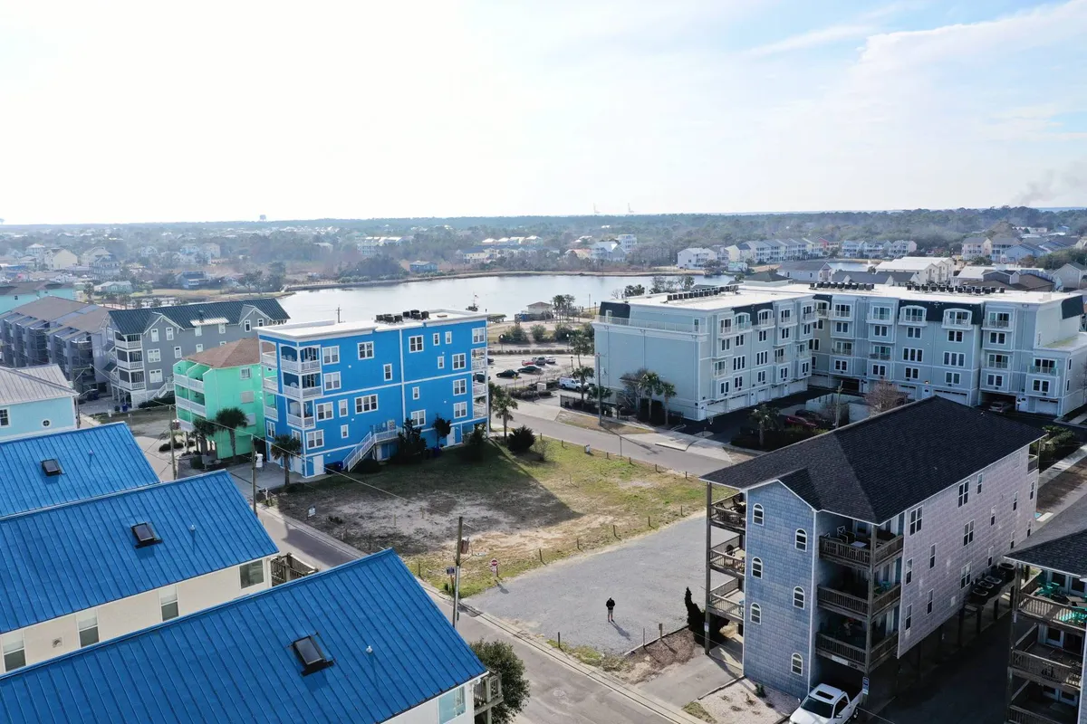 A lively waterfront scene featuring colorful buildings overlooking a calm body of water, with inviting green spaces where people can walk, bike, and gather. The setting feels festive, open, and community-oriented, suggesting a blend of outdoor recreation and local events.
