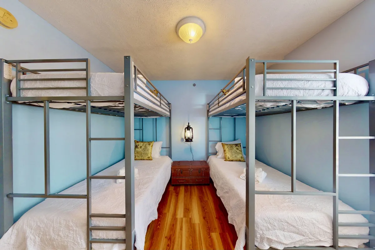 A playful and relaxed bunk room featuring two sets of bunk beds, a lantern-style light, textured bedding, and wooden flooring. The space feels fun and inviting, perfect for kids or teens to enjoy late-night chats and shared adventures.
