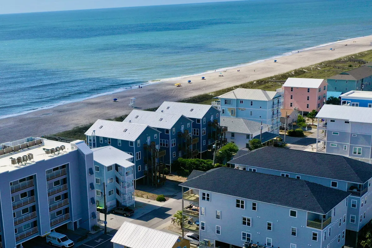 A cheerful beachfront setting with a row of colorful buildings lining the shore, gentle ocean waves, and an inviting sandy beach. The scene evokes a sense of leisure, fun, and accessibility to water sports and beach activities.