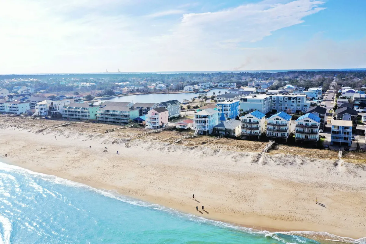 A serene image depicting beachfront properties and sandy shores with gentle ocean waves and distant trees. The scene suggests activities like beach walks, family gatherings, water sports, and sunbathing, all underscored by an atmosphere of relaxation. It hints at sunset views, early morning walks, and local seafood dining experiences.