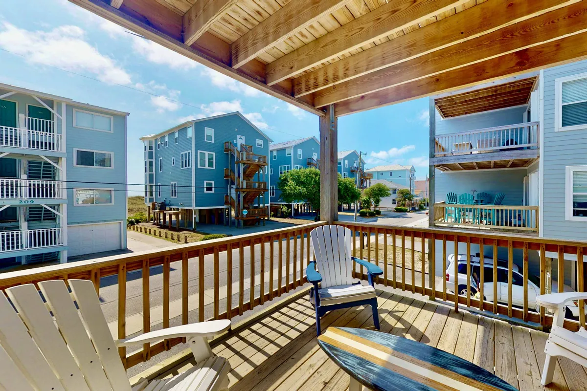This image features a wooden deck with white chairs overlooking the street and blue buildings, suggesting an elevated vantage point. The atmosphere is casual and inviting, ideal for relaxing or socializing while enjoying the view. The perspective highlights the deck's privacy and connection to the surrounding scenery.