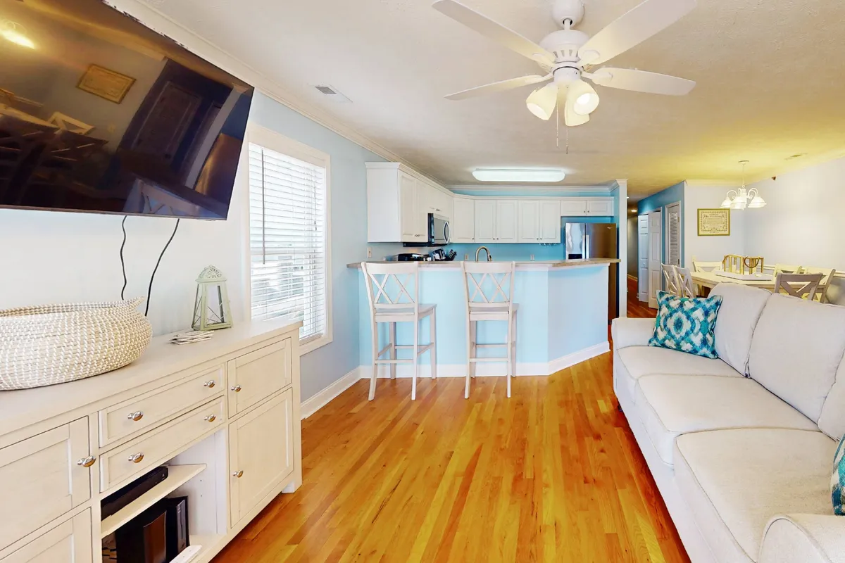 This image showcases an expansive open-concept living space that includes a comfortable sofa with cushions, a kitchen island, and a television, all in one area. The room is filled with natural light, highlighting the cohesiveness between lounging, dining, and cooking spaces. The decor is modern yet welcoming, reinforcing a sense of togetherness and functionality.