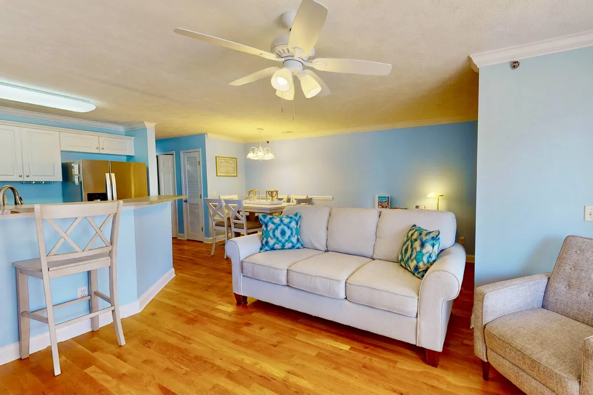 A casual and comfortable space featuring a sofa with decorative cushions, a spacious dining table, and bar stools. The open flow allows for easy movement between lounging, eating, and entertaining, while the decor exudes warmth and an inviting atmosphere for family gatherings or friendly get-togethers.