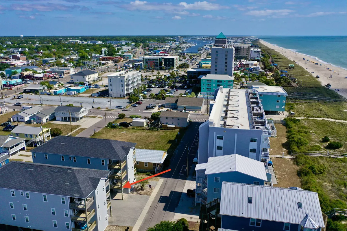 A vibrant exterior scene showcasing the beachfront lined with colorful buildings and an urban layout. People can be seen exploring local shops and dining at nearby restaurants, all set against the backdrop of the ocean. The mood is energetic and inviting, suggesting a place where visitors can enjoy sunset beach walks, local festivals, and delicious fresh seafood.